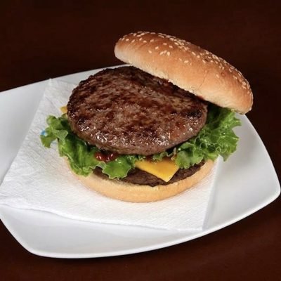 Juicy beef hamburger with lettuce and cheese on a sesame bun, plated on a napkin.