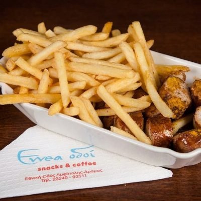 Plate of French fries and sausage bites on a dark wooden table, in a white oval dish with a napkin nearby.